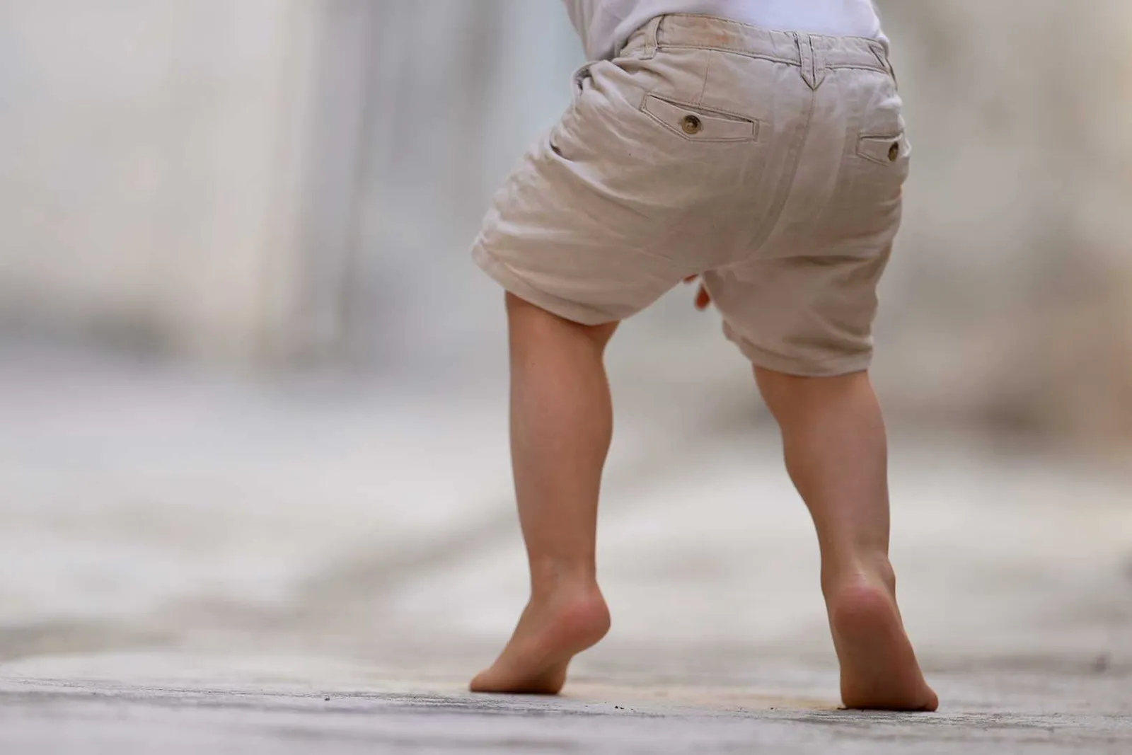 Young child walking barefoot on their toes, seen from behind