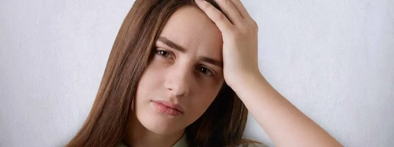 Adult resting a hand against her head, looking drained — visual symptoms often linger after a concussion or brain injury