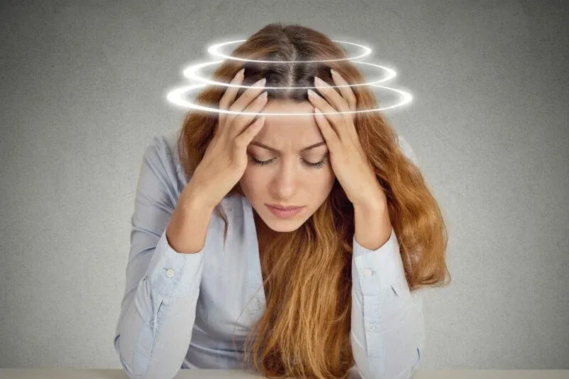Woman holding her head with rings circling above it, illustrating dizziness and a spinning sensation