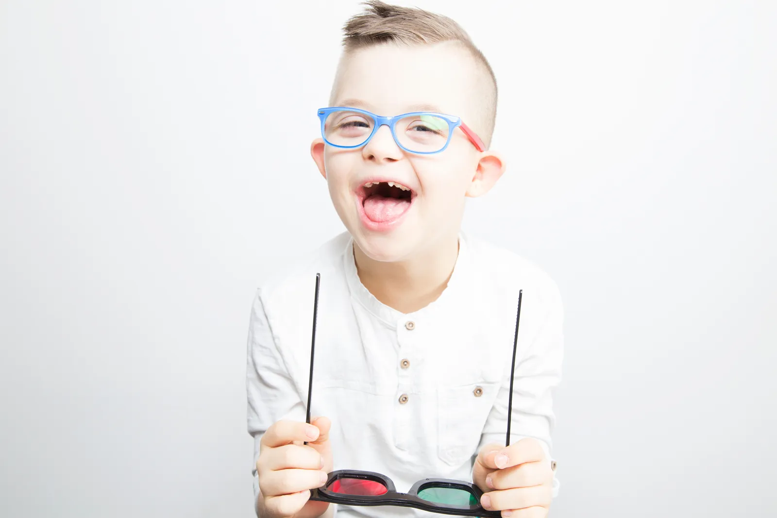 Smiling boy in blue glasses holding a pair of red-green therapy glasses