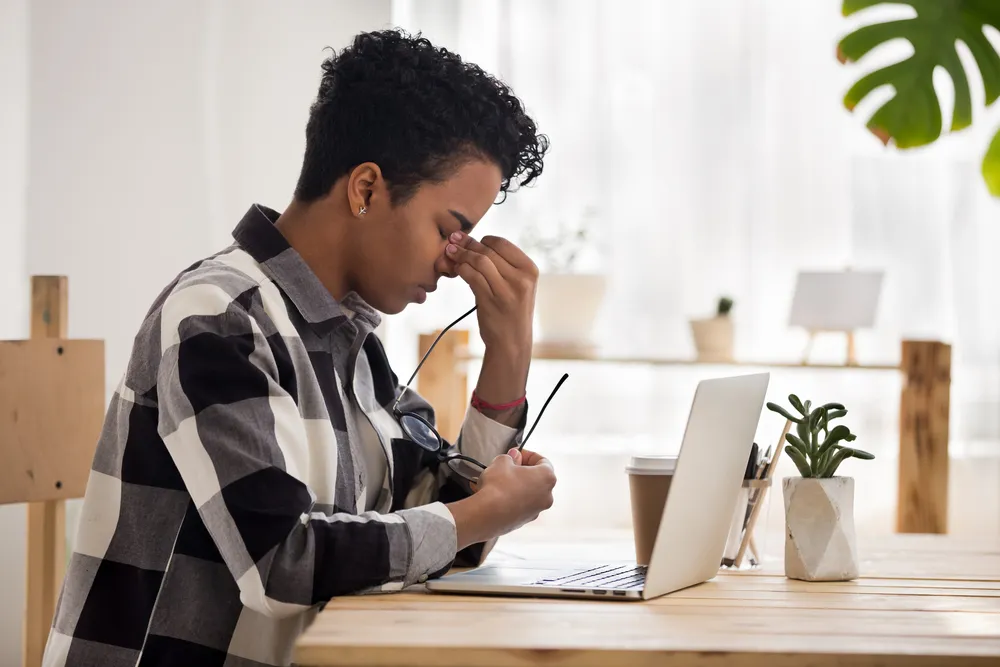Adult at a laptop taking off their glasses to rub tired eyes after a long stretch of screen work