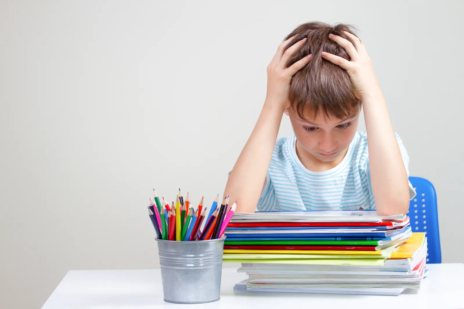 Boy sitting at a desk with his head in his hands beside a stack of schoolbooks