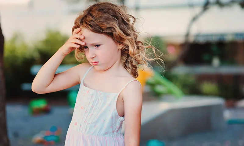 Young girl outdoors holding her forehead with a pained expression