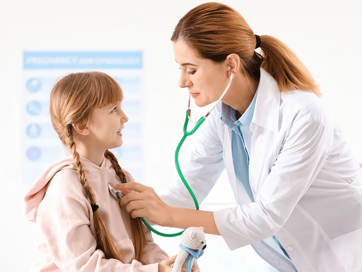 Pediatrician in a white coat examining a smiling school-age girl holding a toy