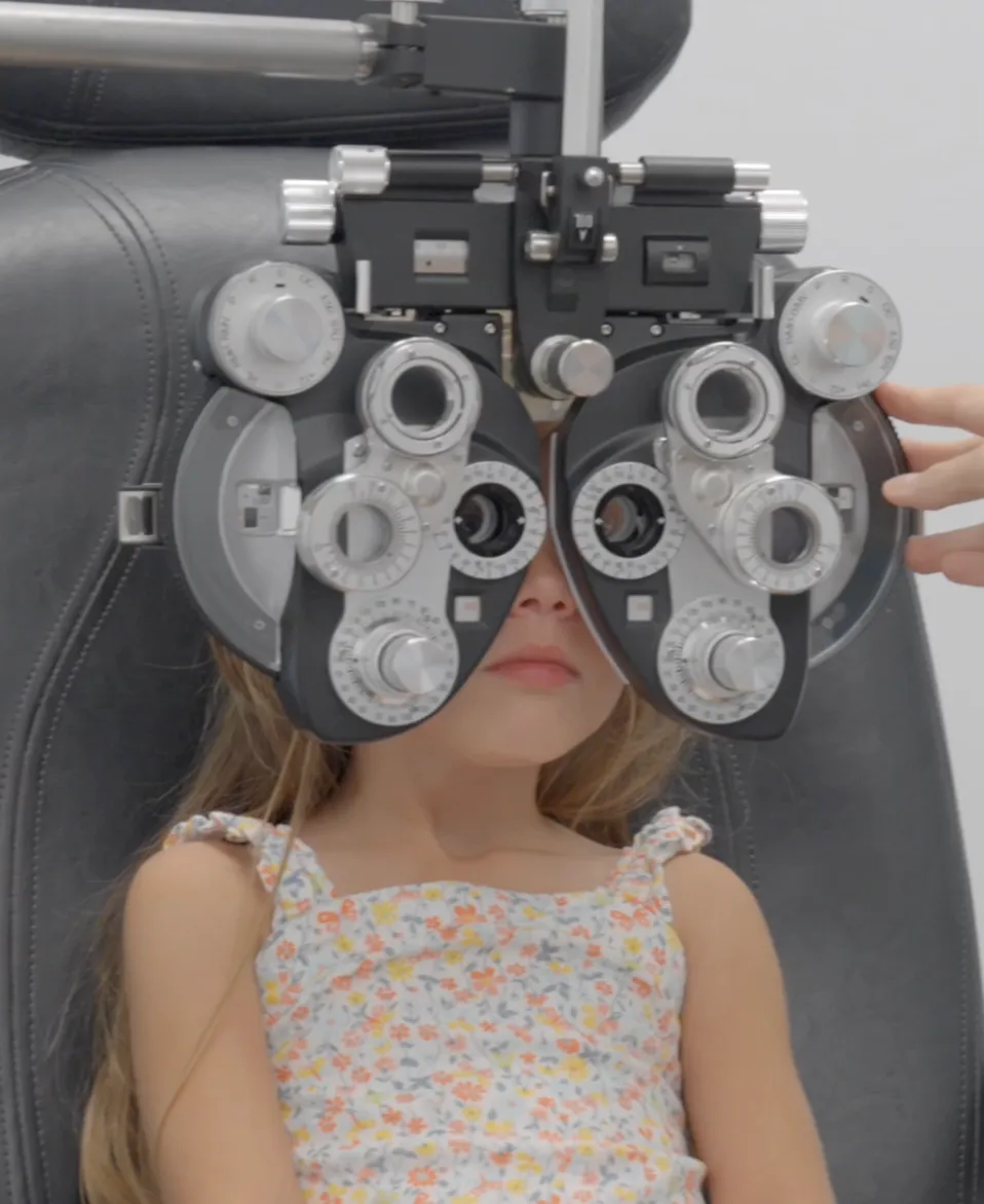 Young girl seated in an exam chair looking through a phoropter during an eye exam