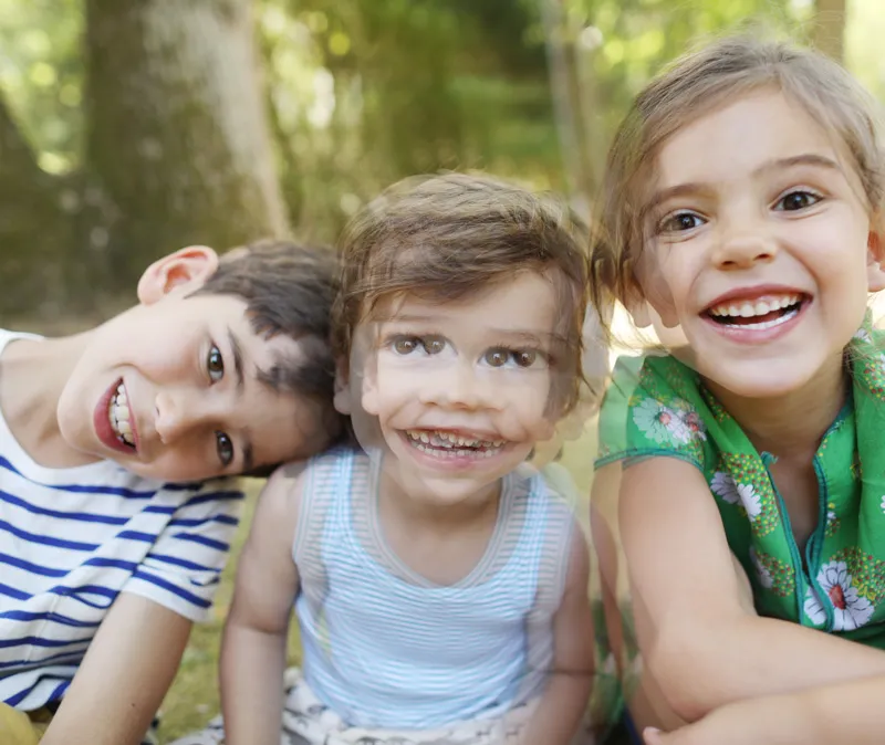 Three smiling children outdoors, the middle child shown doubled to illustrate double vision