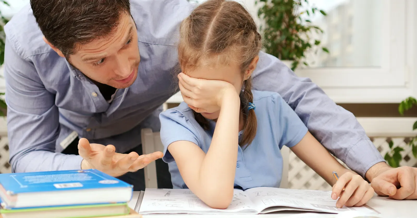 An adult sitting beside a child who is leaning over a book, rubbing their eyes