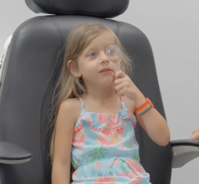 A young child in the exam chair holding an occluder over one eye during a cover test