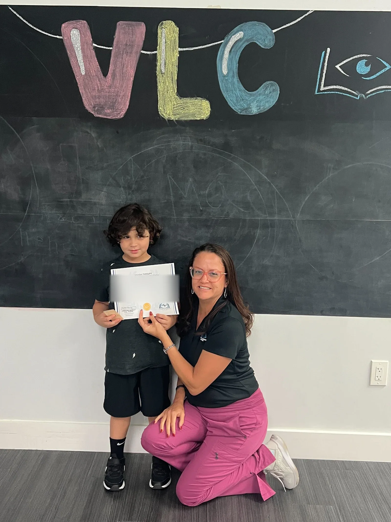 A vision therapy graduate holding their certificate with their therapist