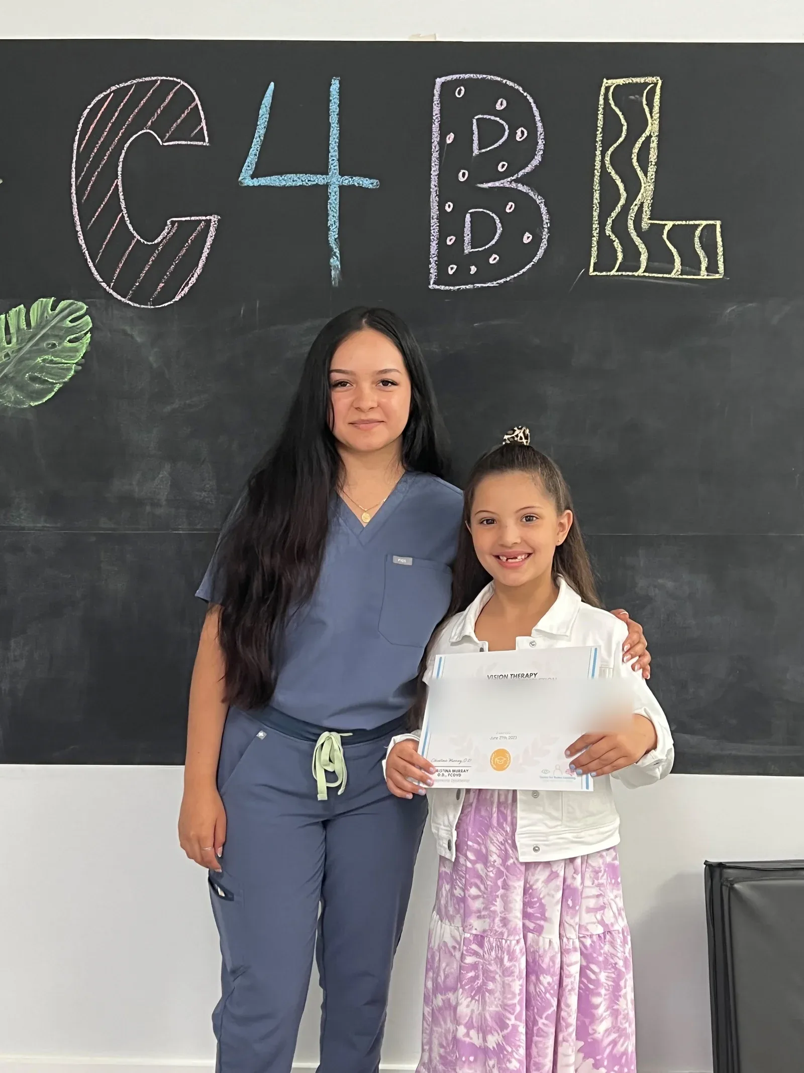 A vision therapy graduate holding their certificate with their therapist
