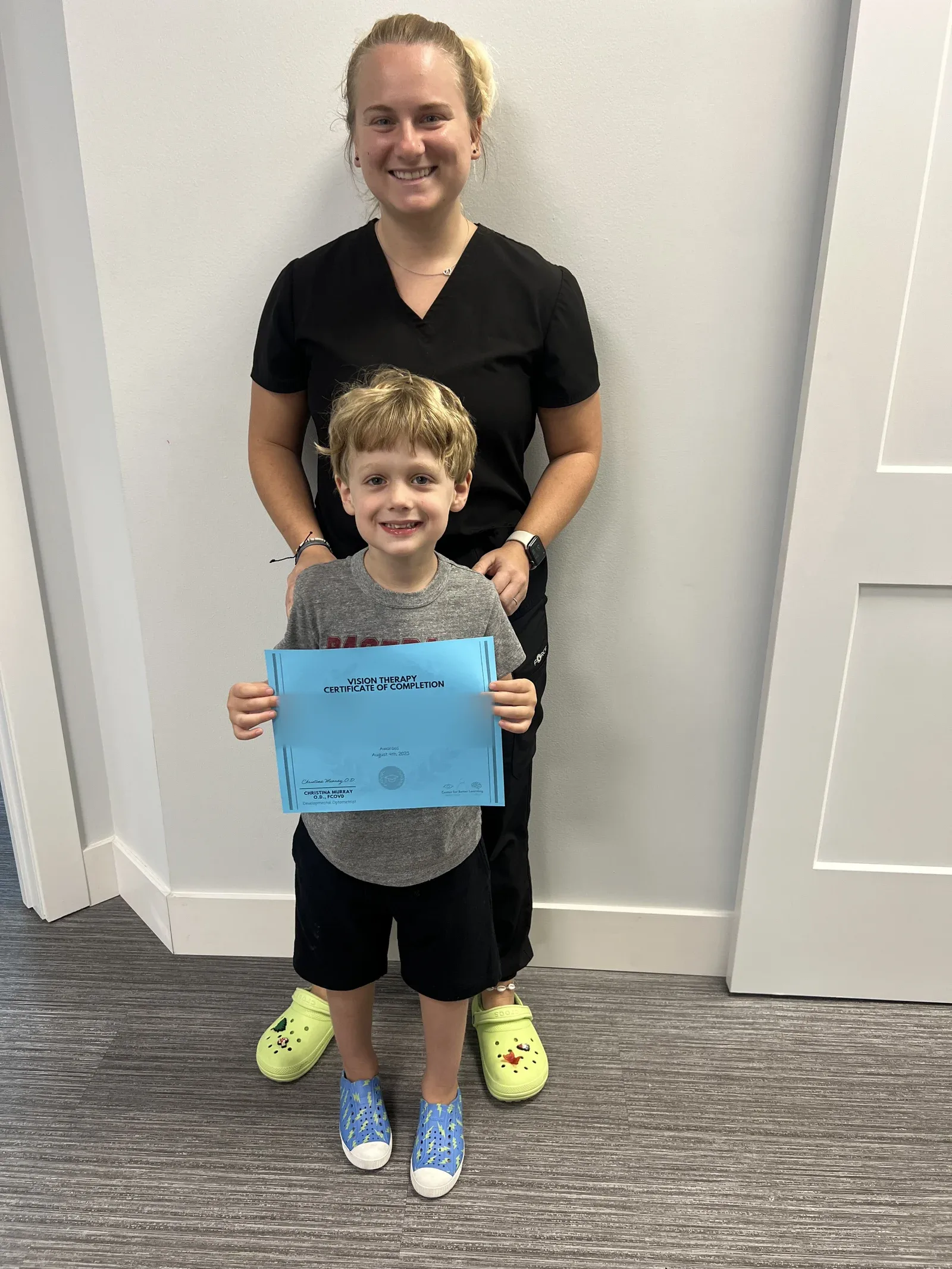 A vision therapy graduate holding their certificate with their therapist