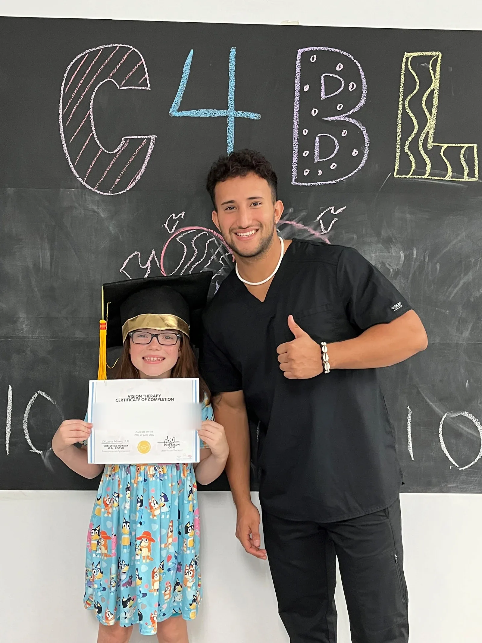 A vision therapy graduate holding their certificate with their therapist