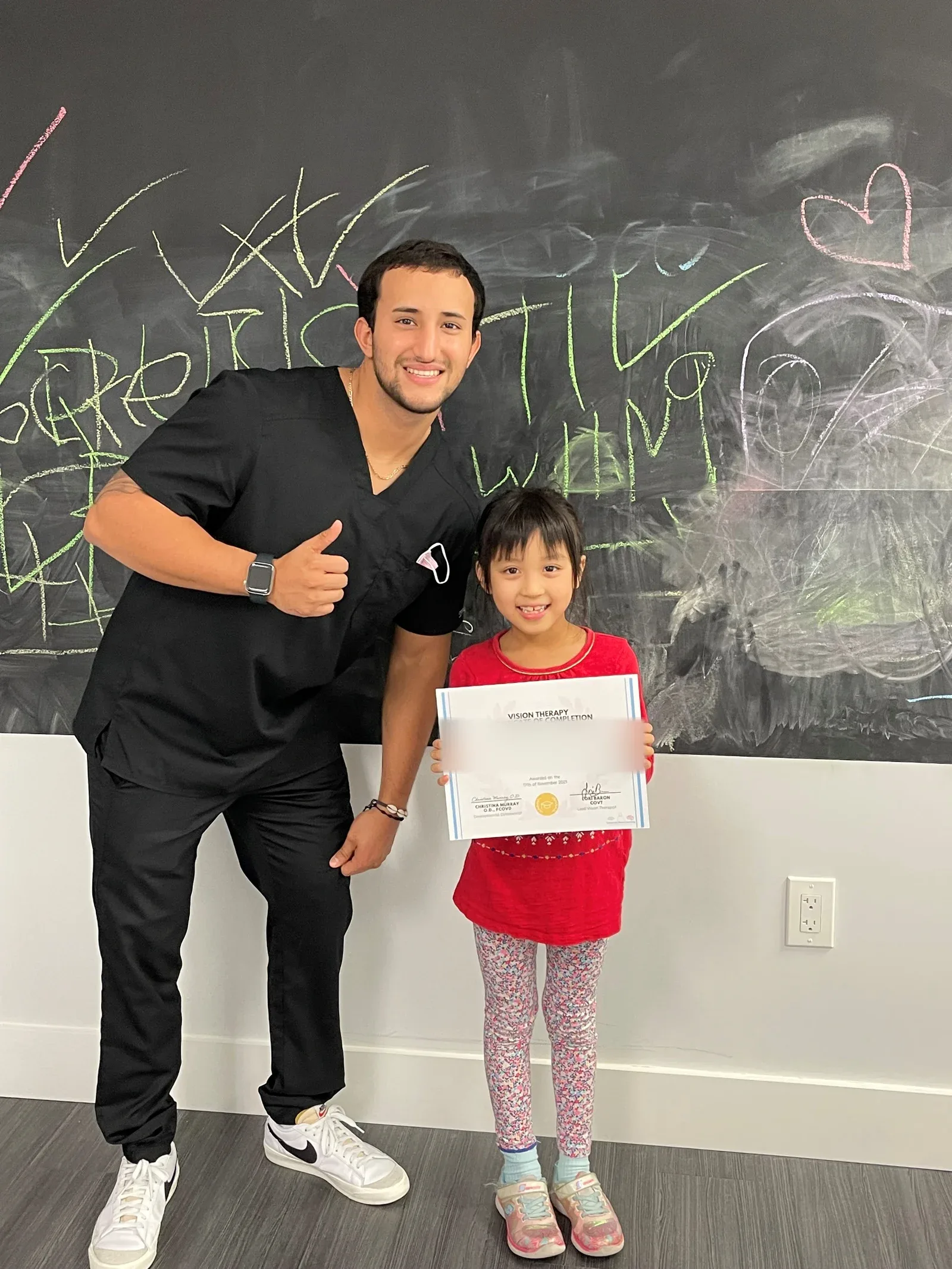 A vision therapy graduate holding their certificate with their therapist