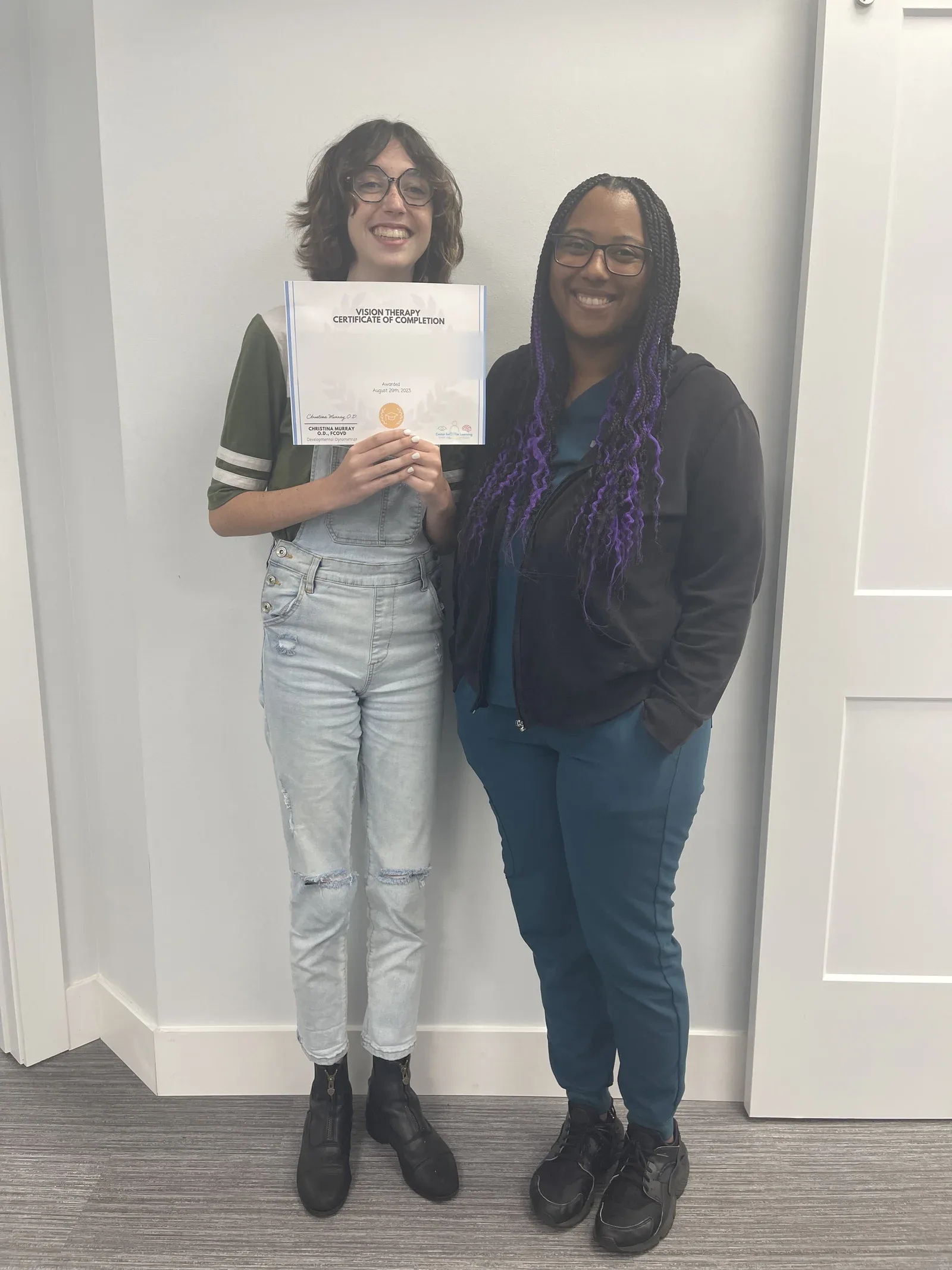 A vision therapy graduate holding their certificate with their therapist