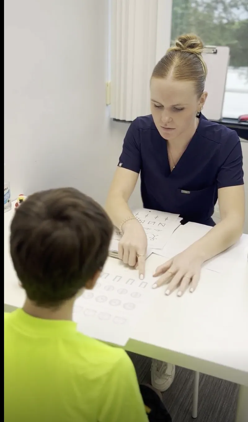 Clinician pointing to a row of shapes on a visual perceptual test worksheet while a boy studies the page