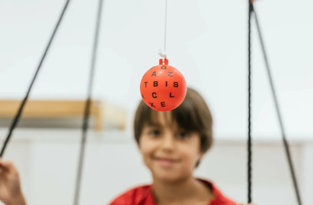 An orange Marsden ball printed with black letters hangs on a string in front of a smiling child during a tracking activity.
