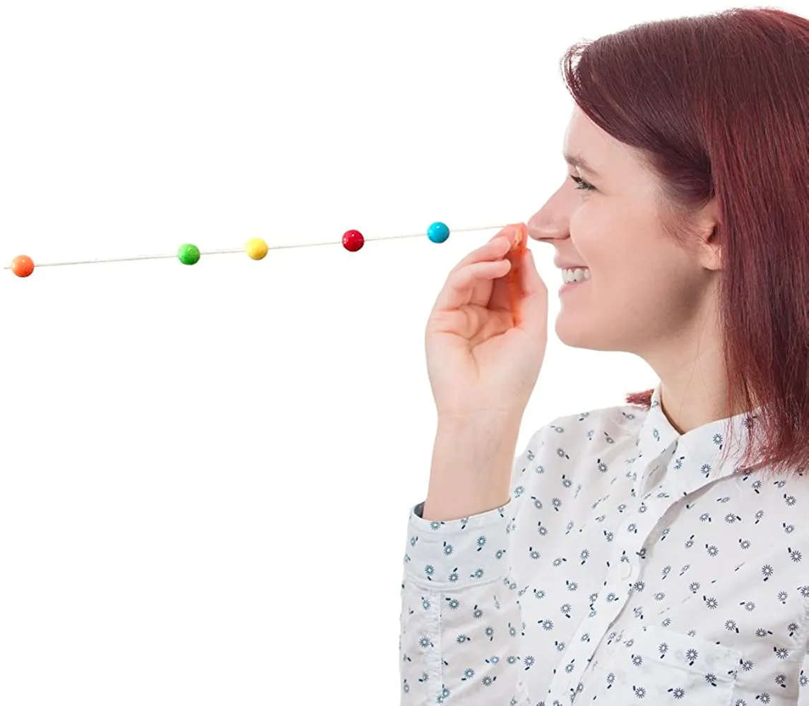 A woman holds one end of a Brock string against the bridge of her nose while colored beads sit spaced along the cord in front of her