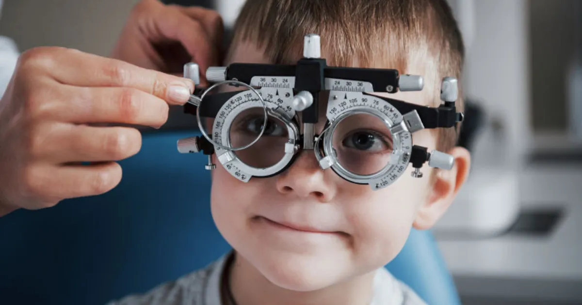 Child seated in an exam chair wearing a trial frame while lenses are changed during a developmental vision evaluation.