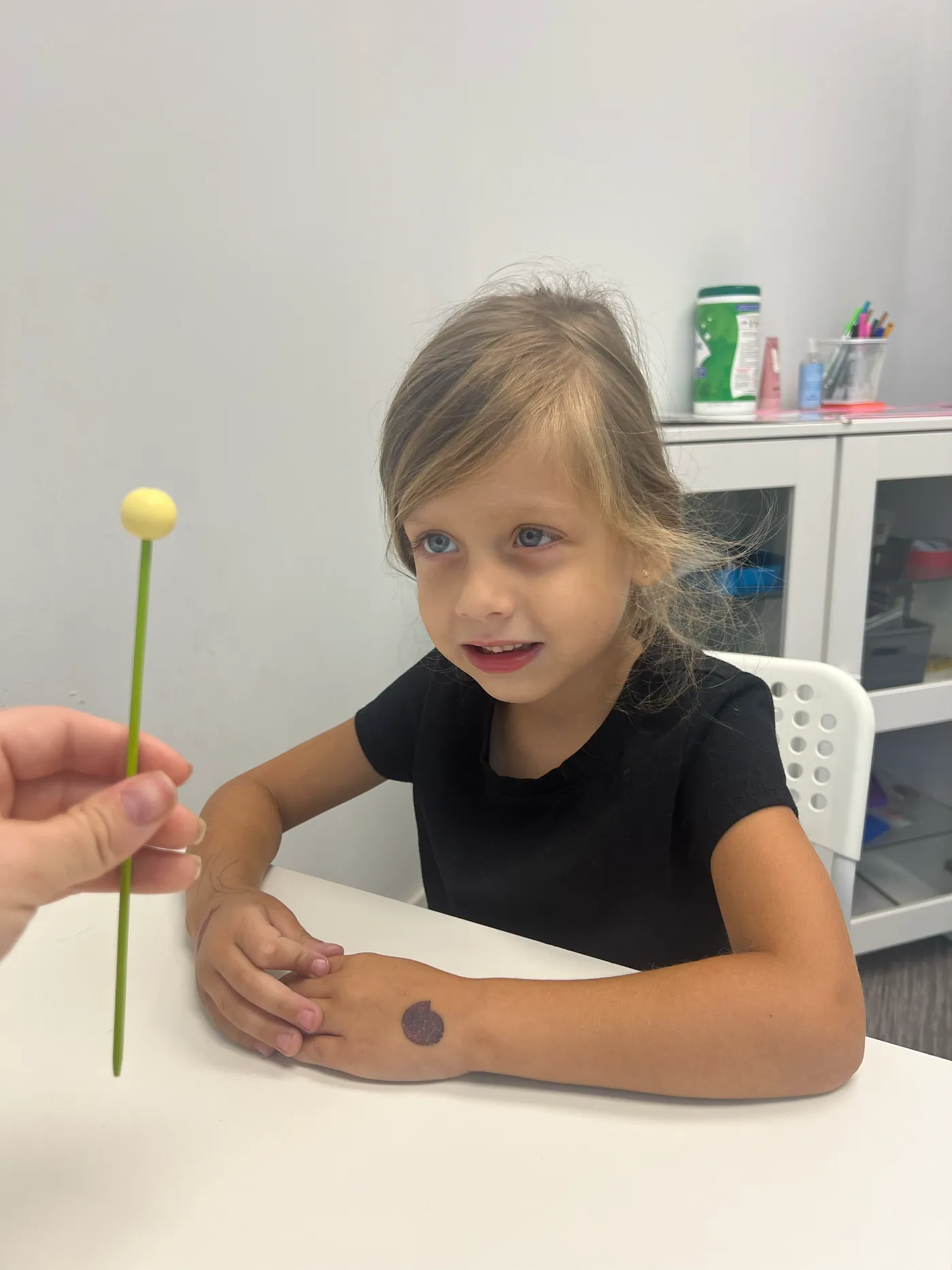 A child sits at a vision therapy table while a therapist holds out a yellow bead on a wand for her to track with both eyes