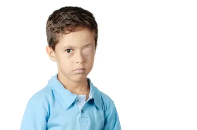 School-age boy in a blue polo shirt wearing an adhesive patch over his right eye, the standard first-line treatment for amblyopia.