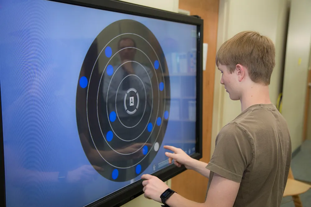A teenage patient reaching for moving targets on a large touch-screen therapy display, the kind of in-office eye-teaming and tracking work the trials tested